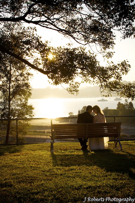 Couple sitting on bench looking at setting sun - wedding photography sydney